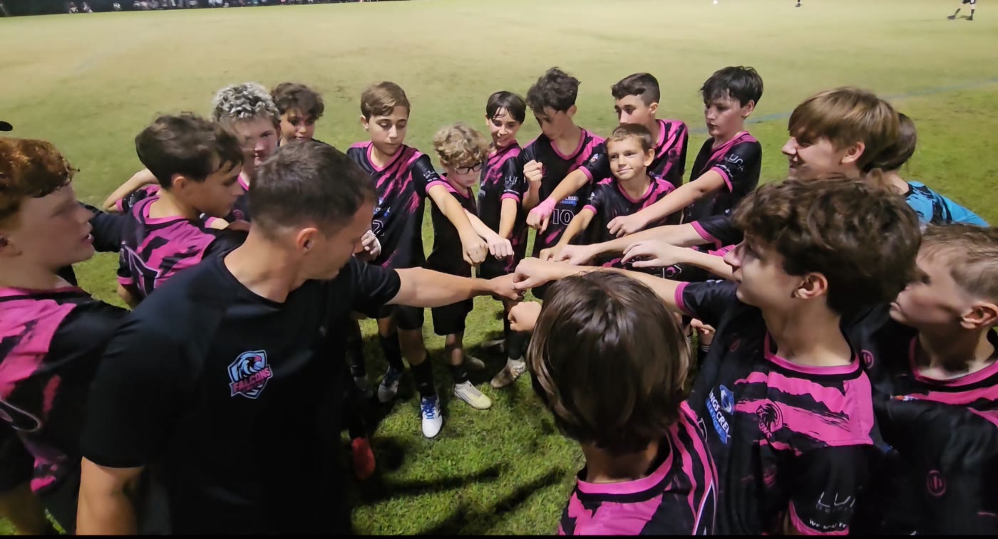 Falcons United players and their coach in a huddle with their hands together in the centre