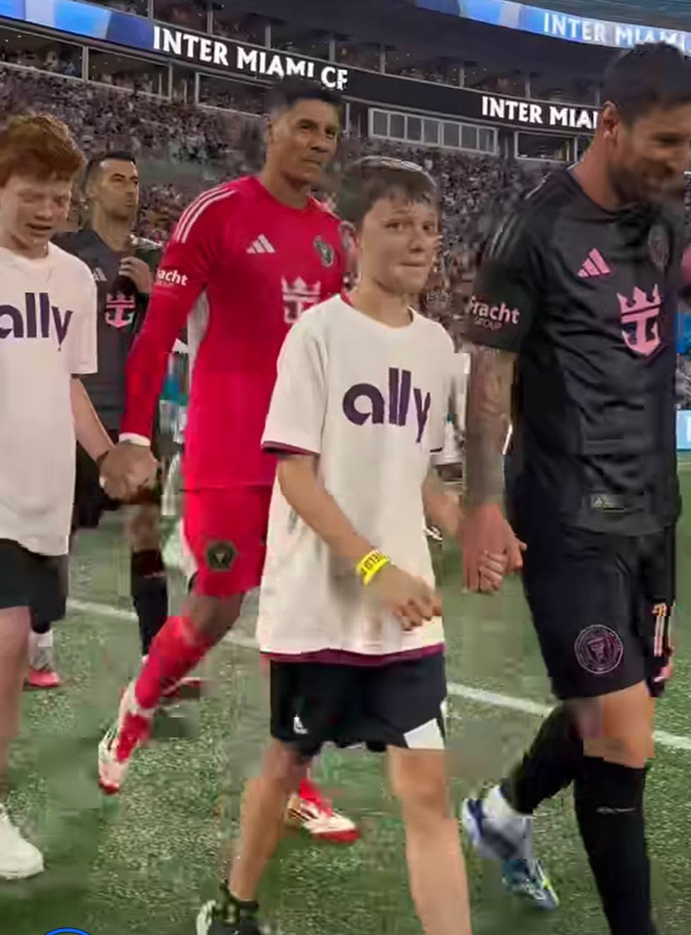 Falcons United players walking out onto the pitch hand in hand with professional players at an Inter Miami match